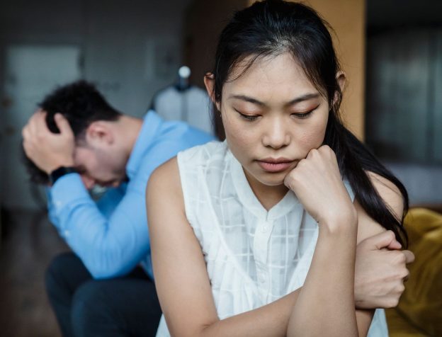 Cặp vợ chồng ngồi hai đầu bàn gỗ, quay lưng nhau trong nhà