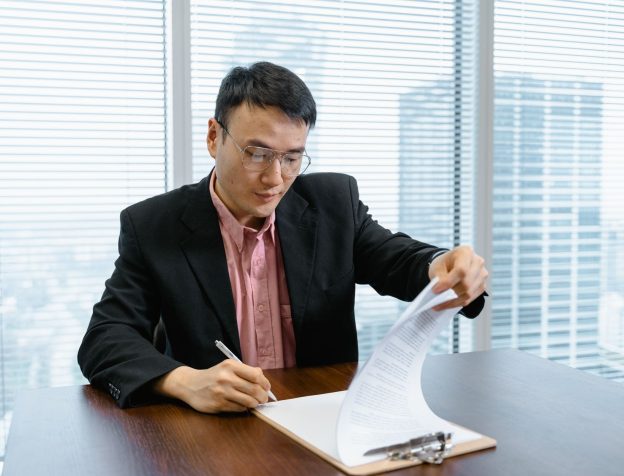 Người đàn ông châu Á cầm bút ký giấy tờ tại quầy tiếp nhận hành chính