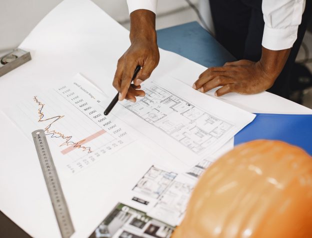 Người đàn ông trung niên đang xem xét kỹ lưỡng một bản đồ giấy lớn tại văn phòng, có thể là bản đồ quy hoạch hoặc sổ đỏ.