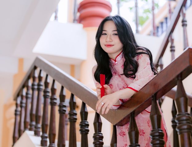 Người phụ nữ trẻ người Việt cầm trên tay một tờ giấy chứng nhận quyền sử dụng đất màu hồng, mỉm cười, trong nhà