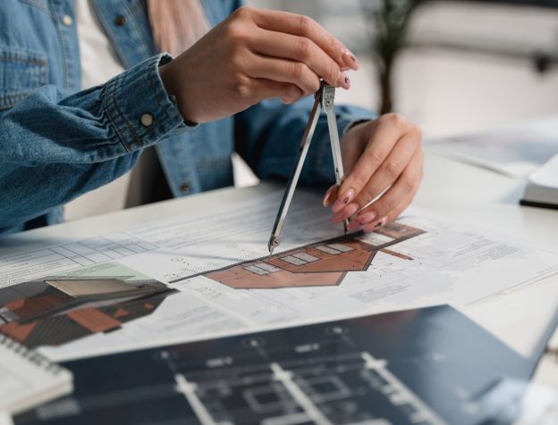Một người đàn ông châu Á đang xem bản vẽ quy hoạch hoặc giấy tờ nhà đất, với la bàn trên bàn