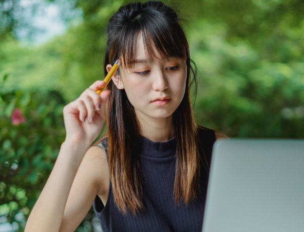 Một người phụ nữ đang ngồi suy tư trước màn hình máy tính, có thể đang xem xét các lựa chọn bất động sản hoặc thông tin thị trường.